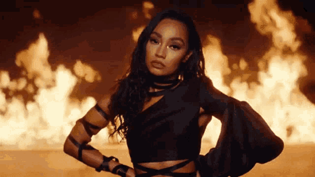 a woman in a black dress is standing in front of a large fire .
