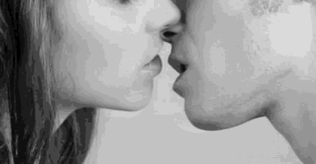 a black and white photo of a man and a woman kissing .