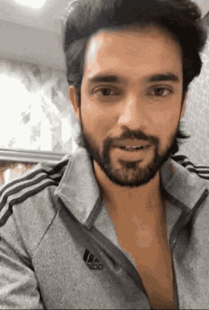 a man with a beard is wearing a grey adidas jacket