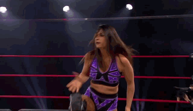 a woman in a purple and black outfit is standing in a ring .