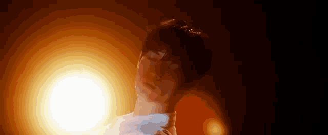 a man in a white shirt is standing in front of a bright light in the dark .