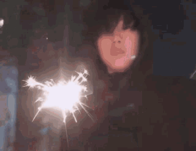 a woman is holding a sparkler in front of her face at night .