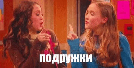 two girls are standing next to each other and one of them is holding a lollipop and the other is pointing at the other .