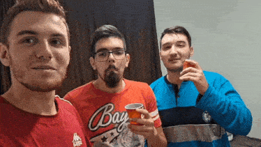 three men are posing for a picture and one of them is wearing a red shirt that says bay