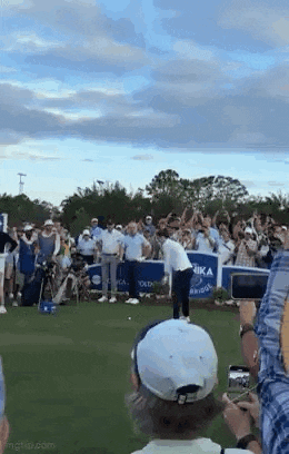 a man is swinging a golf club at a golf ball while a crowd watches .