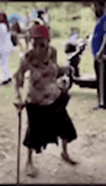 an elderly woman is walking with a cane in the dirt .