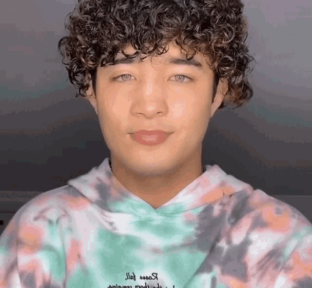 a young man with curly hair is wearing a tie dye hoodie that says ' animals ' on it
