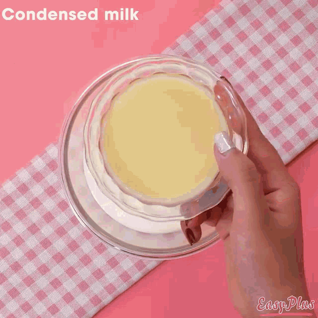 a woman 's hands are reaching into a bowl of whipped cream on a pink table cloth .