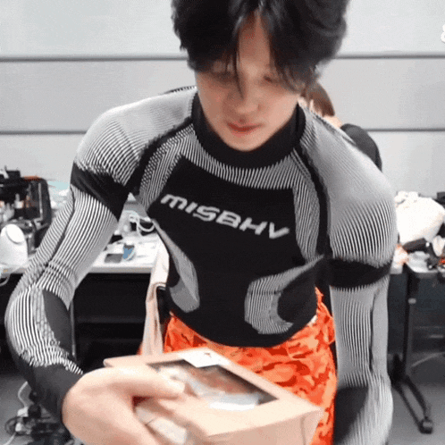 a man wearing a shirt that says misbhv holds a box