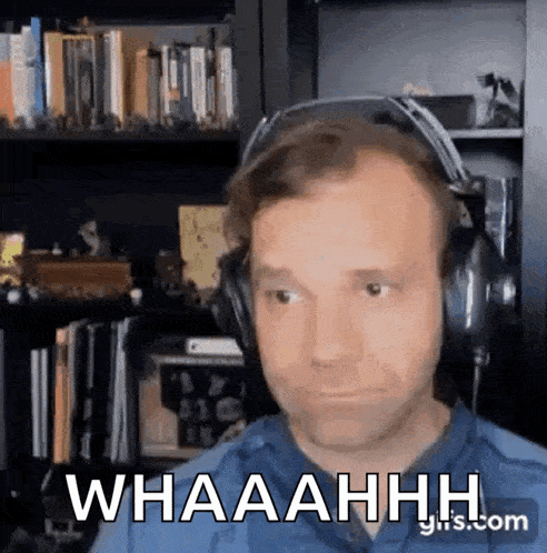 a man wearing headphones is sitting in front of a bookshelf and saying whaaahhh .