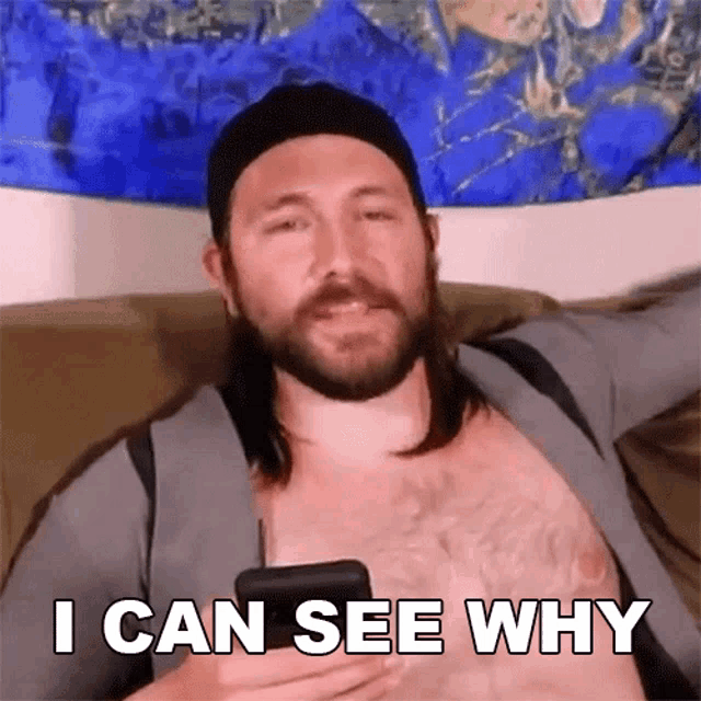 a shirtless man sitting on a couch holding a cell phone and saying " i can see why "