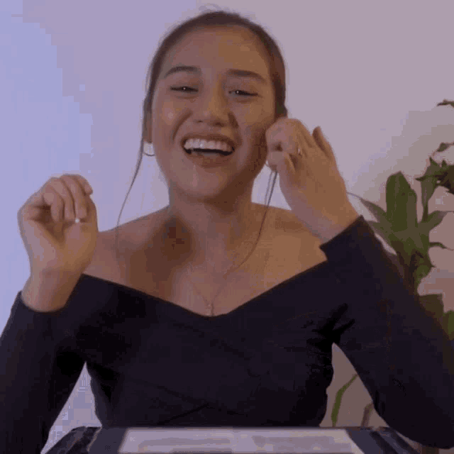 a woman in a black off the shoulder top smiles
