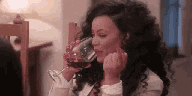 a woman is drinking a glass of wine at a table .