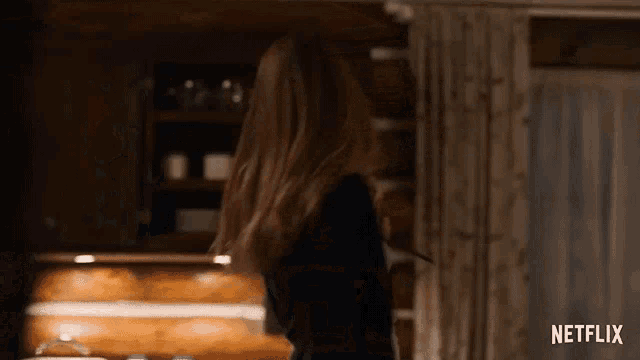 a woman is standing in a kitchen with her hair blowing in the wind and a netflix logo in the corner .