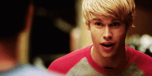a young man with blonde hair is wearing a red shirt and a gray shirt .