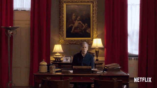 a man sits at a desk in front of a painting and a sign that says netflix