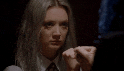 a woman with gray hair and a white shirt and tie holds her hands together