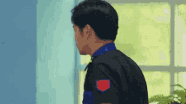 a man in a black shirt with a red patch on the sleeve is standing in front of a window in a room .