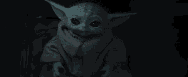a baby yoda from star wars is sitting in a dark room .