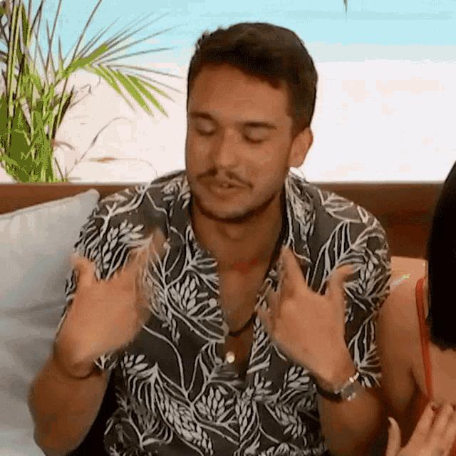 a man in a floral shirt is sitting on a couch with a woman and making a funny face .