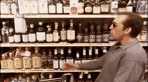 a man in sunglasses is standing in front of a shelf full of liquor bottles .