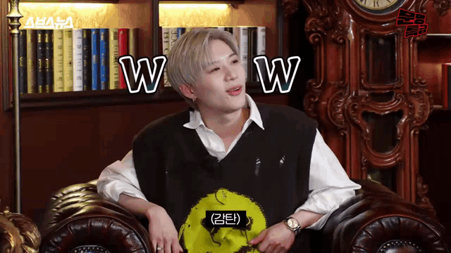 a young man is sitting on a couch with a clock in the background and says wow