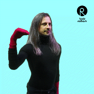 a man with long hair and red gloves stands in front of a blue background that says rozbark