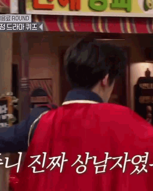 a man wearing a red cape is standing in front of a sign that says round .