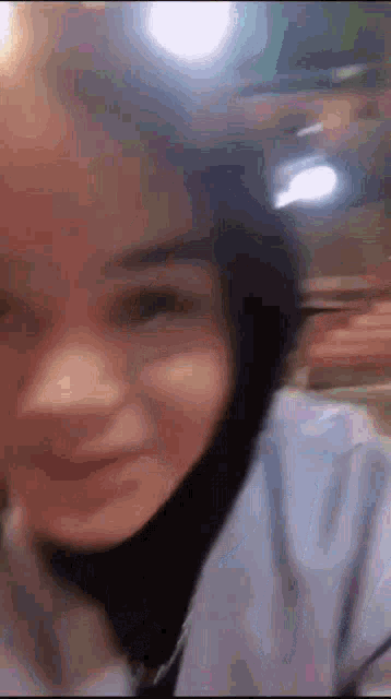 a close up of a woman 's face with a blurry background . she is wearing a hijab and smiling .