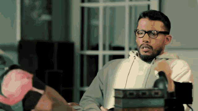 a man wearing glasses sits at a table with a box that says 000