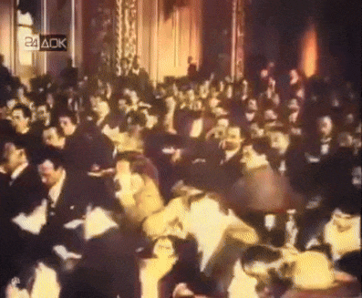 a crowd of people sitting in a theater with a 24 aok sign in the background
