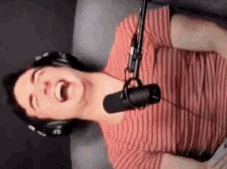 a man wearing headphones and a red striped shirt is laughing into a microphone