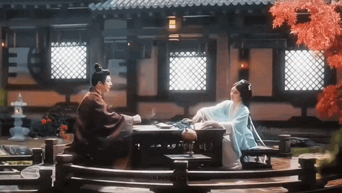 a man and a woman sit at a table in front of a building .