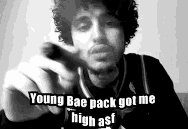 a man with curly hair and a beard is pointing at the camera and says young bae pack got me high asf