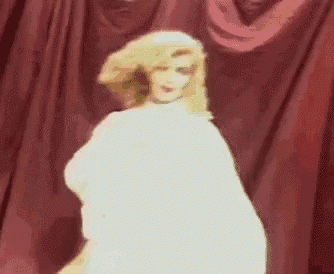 a doll is sitting on a stage in front of a red curtain with a light coming out of it .