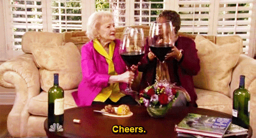 two women are sitting on a couch toasting with wine glasses and cheers .