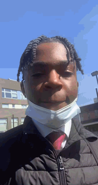 a young man wearing a mask and a jacket looks at the camera
