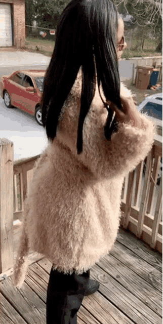 a woman wearing a fur coat is standing on a deck .