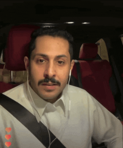 a man wearing ear buds and a mustache is sitting in a car