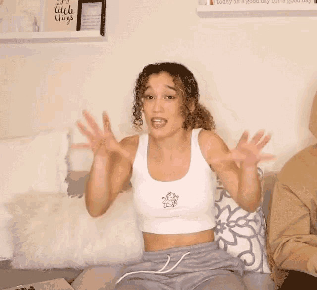 a woman is sitting on a couch with her hands in the air and a sign that says little things