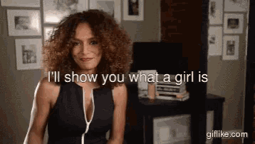 a woman with curly hair is standing in a room and says i 'll show you what a girl is .