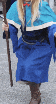a woman in a blue cape and boots holds a cane