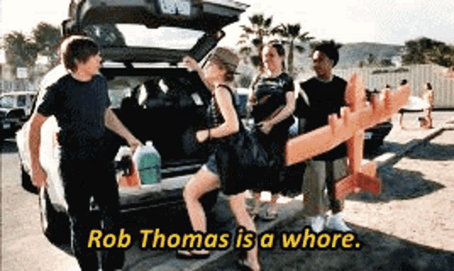 a group of people standing in front of a car with the words rob thomas is a whore on the bottom