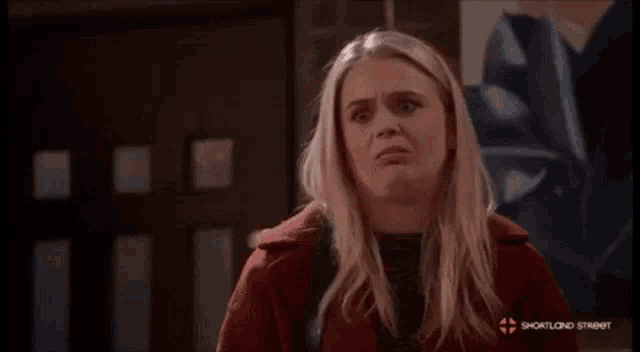 a woman in a red coat is making a funny face in front of a painting .