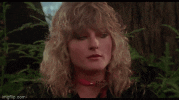 a woman with blonde hair and a red choker is standing in the woods .