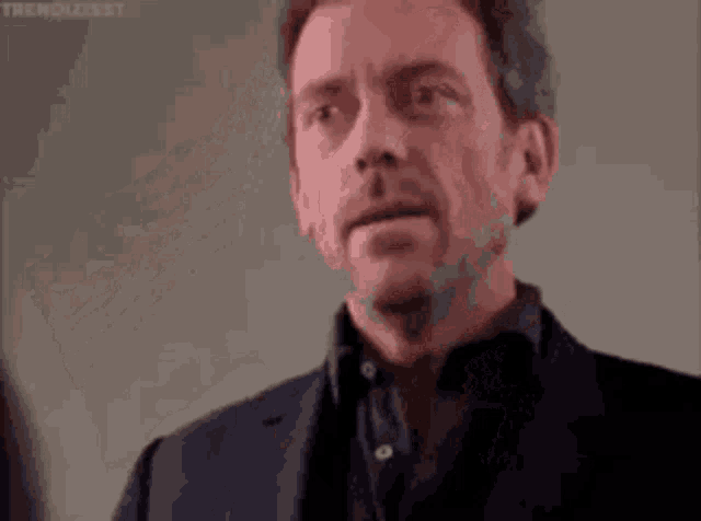a man in a suit is making a funny face with his eyes closed and his hands in the air .