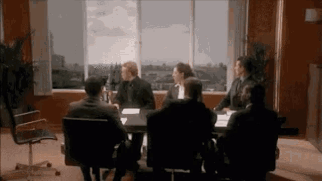 a group of business people are sitting around a table in a conference room .