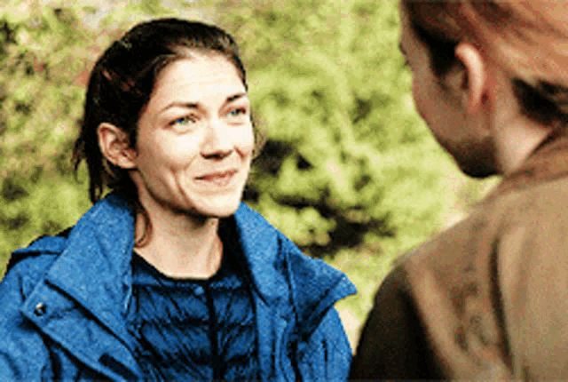 a woman wearing a blue jacket is smiling while talking to another woman
