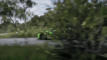 a green car is driving down a road surrounded by trees and grass