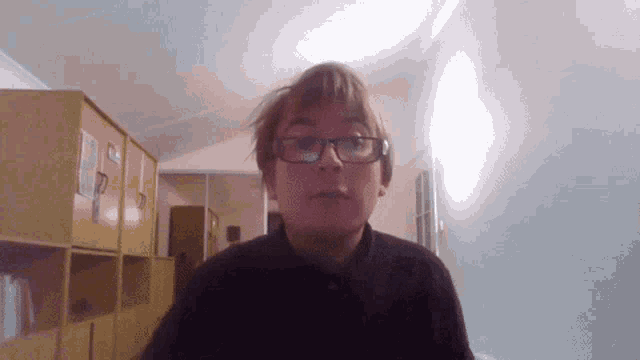 a man wearing glasses and a black shirt stands in a hallway
